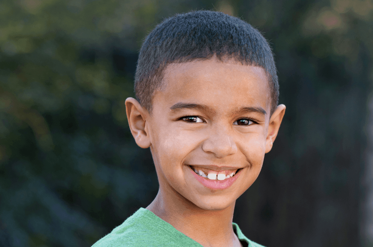 School-aged boy standing outside and smiling at the camera